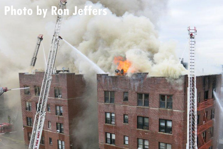 Multiple master streams and aerial devices pour water on a fire in an apartment building in Passaic as flames vent through the roof.