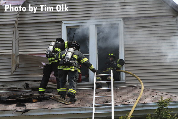 Firefighters advance a hoseline up a ladder and into a window during a house fire.