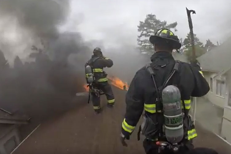 Oakland firefighters on the roof of a house fire