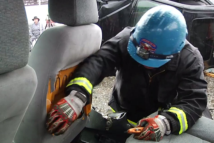 Firefighter using a blade to remove the upholstrey from a vehicle seatback