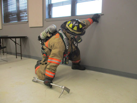 (2) Searching and staying low because of conditions require orientation to a wall to help facilitate locating windows. Sweep high while holding the halligan bar to the ground in the opposite hand. Reach wide and sweep with the tool as you move forward. If you need to investigate something you may have found, feel it with a gloved hand. Use hands to identify victims, not tools. 