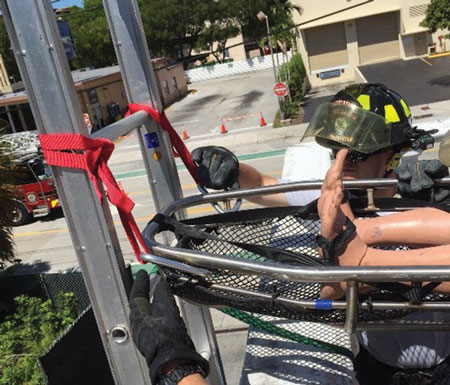 <b>(12-13) </b>On the command of the operations officer, four rescuers raise the basket and move it toward the departure point. Two rescuers near the foot end attach the basket to the webbings on the ground ladder. Do not let the rescue basket sit on the ground, or it will add too much friction until the basket is over the edge. Attach the basket so it is about two feet off the ground. 