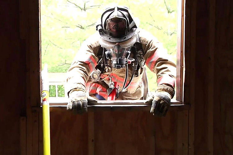 A firefighter makes entry through a window