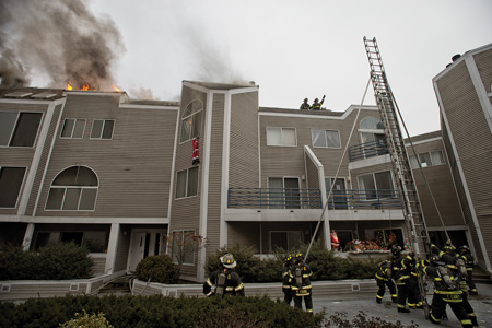 (4) Members raise a Bangor ladder to the roof as a secondary means of egress. Knowledge of the building and its limited access makes it necessary to use different tactics and tools. 