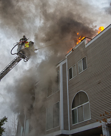 (5) Fire is showing through the roof from vertical and horizontal fire spread. The tower ladder is used to knock down visible fire. 