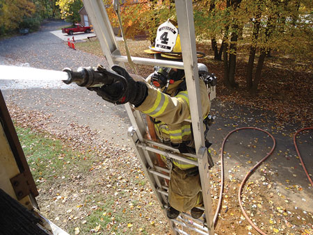 (1) The hose is properly secured with two hose straps using the “in-and-out” method of rigging. The strap is lashed to the hose, then extended upward inside the ladder toward the building and then brought outside the ladder away from the building and hooked over the rung two rungs up. The firefighter is using a leg lock on the side opposite of the hoseline. <i>(Photos by author.) </i>