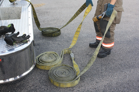 (4) The firefighter is preparing to deploy 150 feet of line. He lays the three rolls on the ground and grabs the coupling between the second and third shot of hose. The nozzle is in his other hand. 