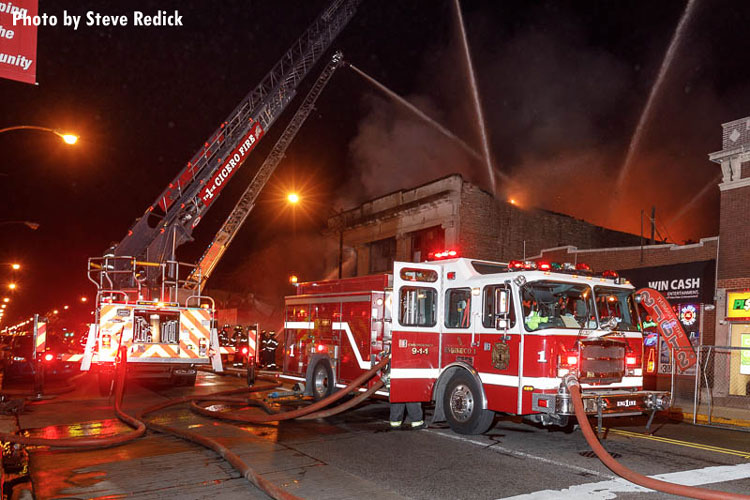 Cicero firefighters and fire apparatus at the scene as master streams are applied to a vacant building