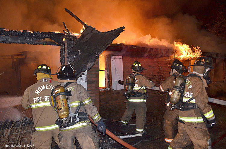 Firefighters pull hoselines at the scene of a house fire