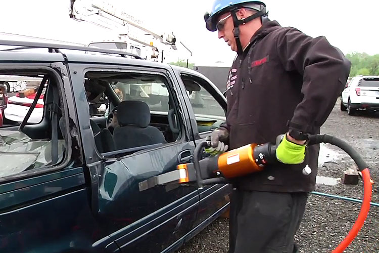 Firefighter with a hydraulic spreader attacks the side door of a minivan