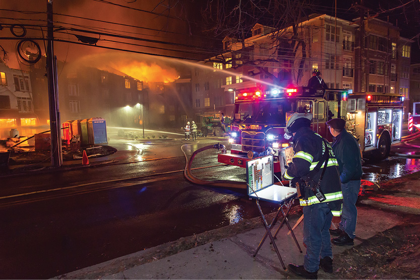 (6) The first-due Engine 32. The incident commander and the Union County mutual-aid coordinator (center) are assessing the stability of the fire wall. Four additional LPG tanks are being cooled (left). 