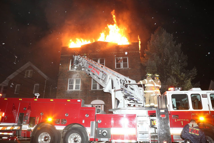 Firefighters on an aerial device as fire vents through the roof of a building