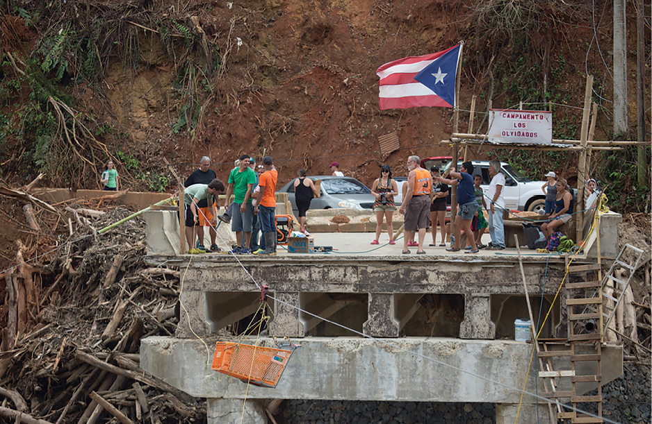 (1) Villagers collect on bridge remnants to receive needed supplies in Utuado, Puerto Rico. (Photo by Andrea Booher/FEMA.)