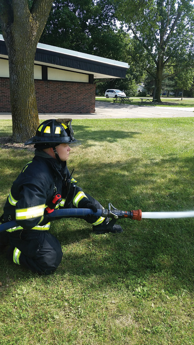 (5) One of the many nozzle positions. Vital points include keeping the nozzle out front and at arm’s length, the hand behind the coupling, and the hand/arm pinned to the side or hip. One knee is up; one knee is down, with a wide base for stability and range of motion. Whatever the stance, it should be comfortable to flow for up to one minute without fatigue and allow for the nozzle firefighter’s mobility and stability.