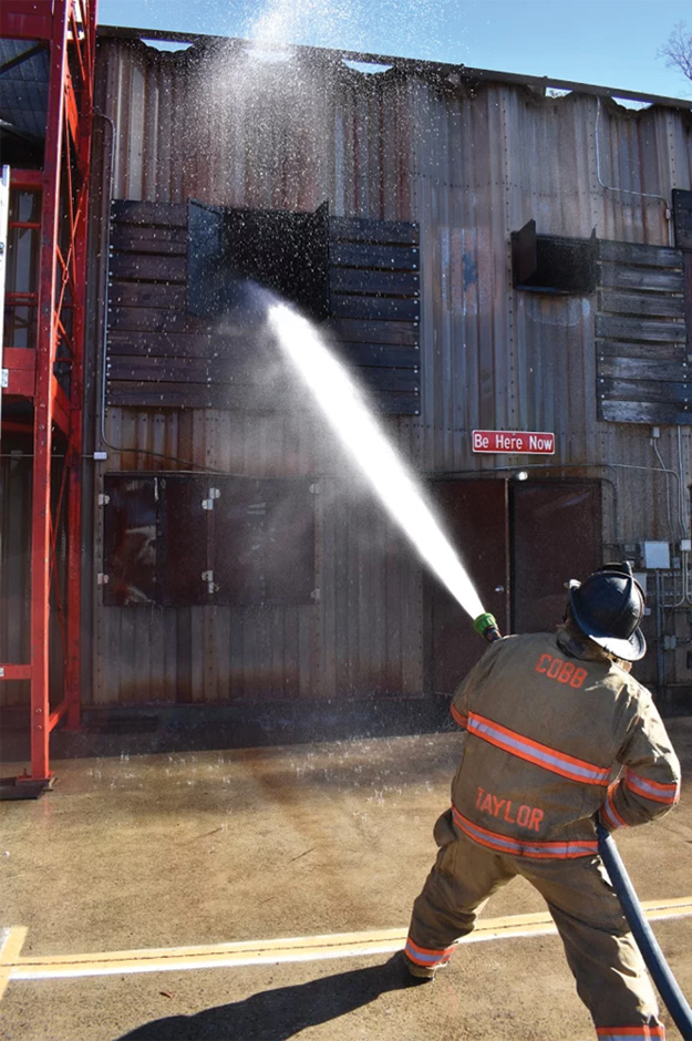 (2) Because this firefighter is standing too far away from the building, the stream is not at the proper angle for stream distribution. The water droplets are missing the portion of the room closest to the window. 