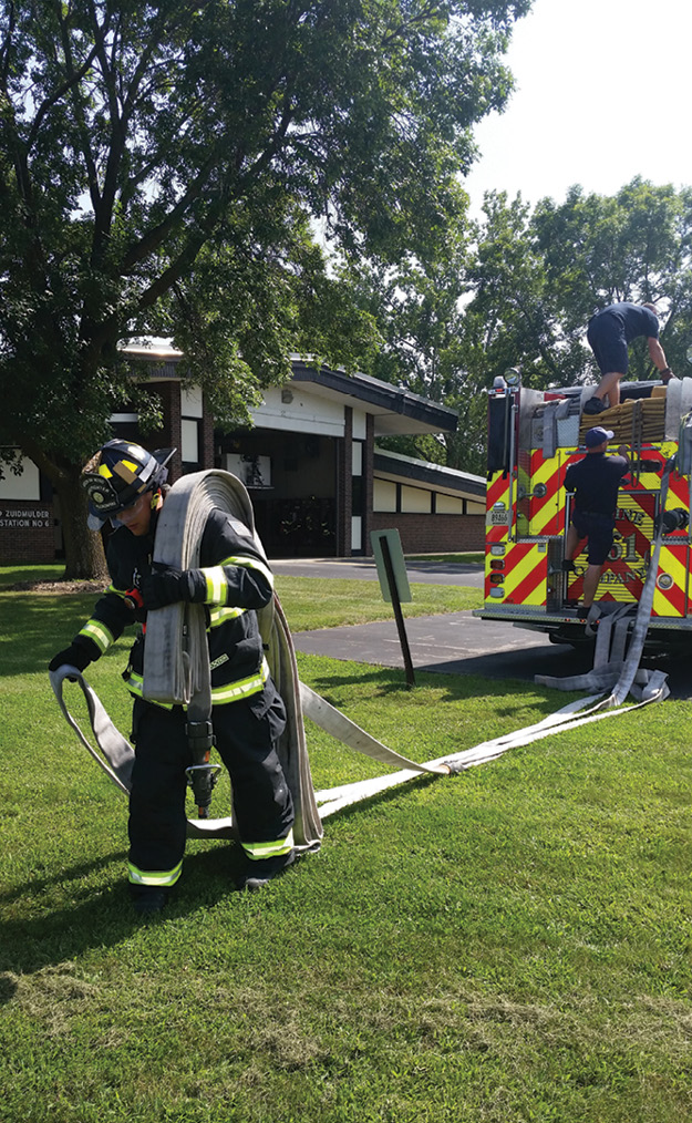 (4) Working from the rear static bed is sometimes beneficial. It usually allows for an expanded menu of lines—in this case, 1¾- and 2½-inch handlines of various lengths. Here, the firefighter is stretching a 250-foot length of 2½-inch hose outside the reach of a preconnected line on this engine. He is shouldering 100 feet of hose and is followed by a drag of 150 feet of lead-out hose—a common single-firefighter stretch for large or medium fire departments in this district. The operator has already prepared the new discharge and knows the length of the stretch from communicating with the firefighter or counting the remaining flakes on the bed.