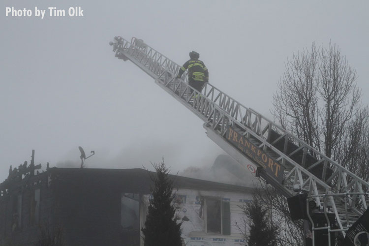 A firefighter ascends an aerial device over a charred building