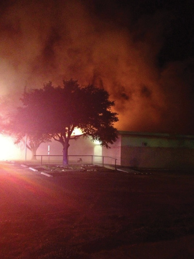 (1) During the Bryan, Texas, incident, the fire, which was initially seen at the A/B corner, spread laterally by means of concealed ceiling spaces. The main entrance was on the A side near the A/D corner. This is the view from the northeast near Command’s location at 2329 hours. Engine 1 is inside, and one positive-pressure ventilation fan is at the doorway. Flames are visible above the A/B corner. (Photos 1-2 courtesy of the Texas State Fire Marshal’s Office Firefighter Fatality Investigation.) 