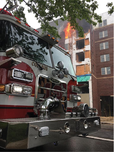 (2) Fire in the sixth-floor apartment of origin. Note the exposed exterior sheathing, the fire directly impinging on the construction lift, and the floor-to-ceiling appliance loading openings. (Photo by Ron Humberson.) 