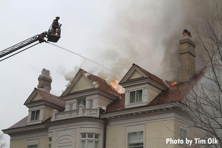 Firefighters pour water on flames venting through the roof of a large home