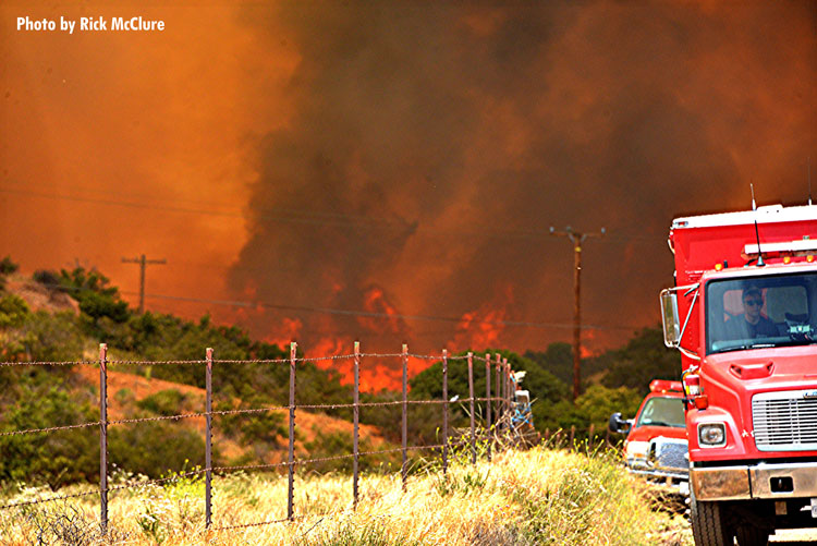 Fire trucks with brush fire raging in the background