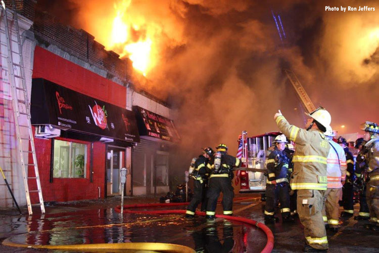 Firefighters scramble with flames and smoke coming from a building