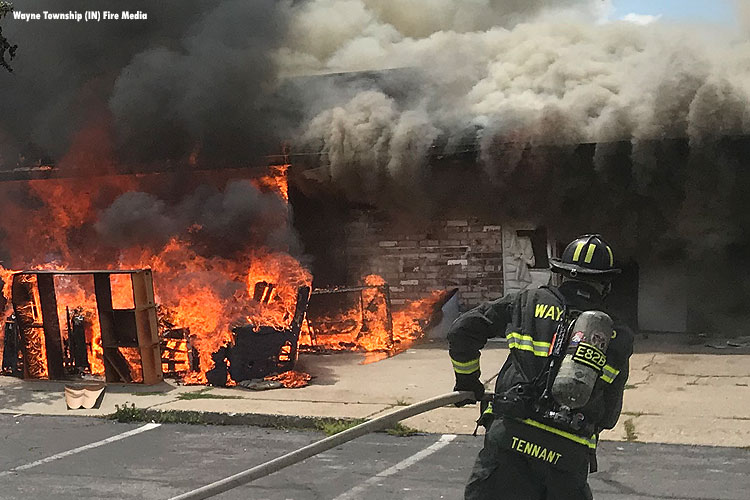 Firefighter dragging a hoseline as fire rages in a building