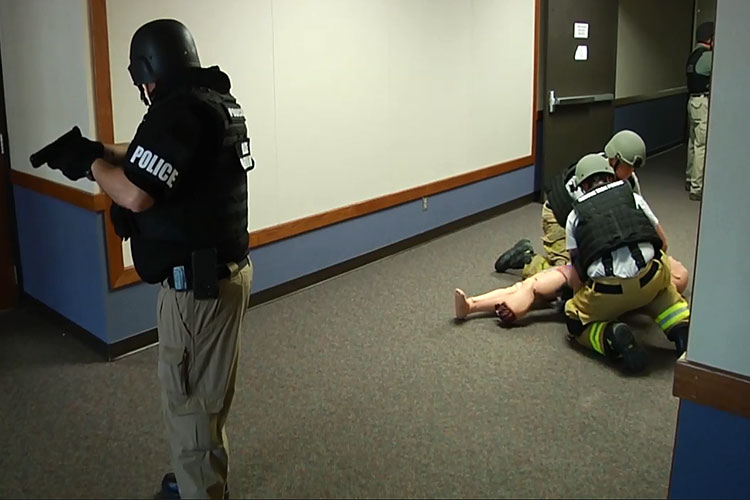 Law enforcement officer stands guard as EMTs attend wounded patient