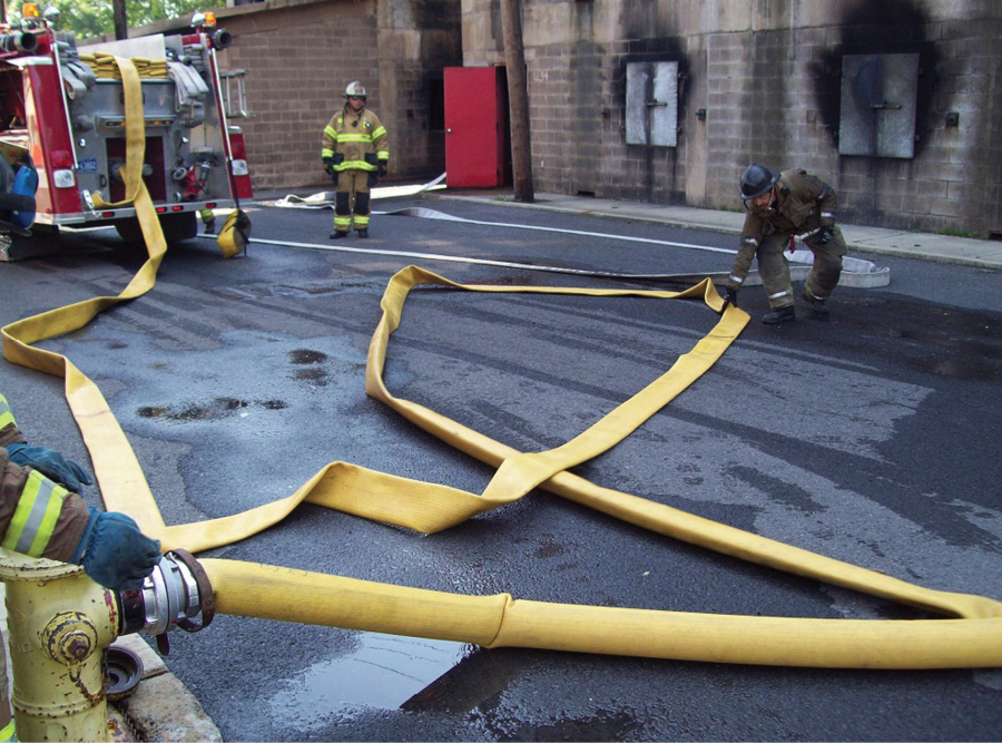 A firefighter flaking out the supply line in a figure eight shape, which will allow the hose to become fully charged and ensure large, smooth bends in the line.