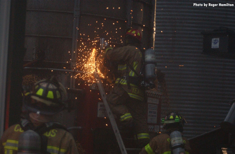 Firefighters use power saws to make entry to grain dryer to access fire