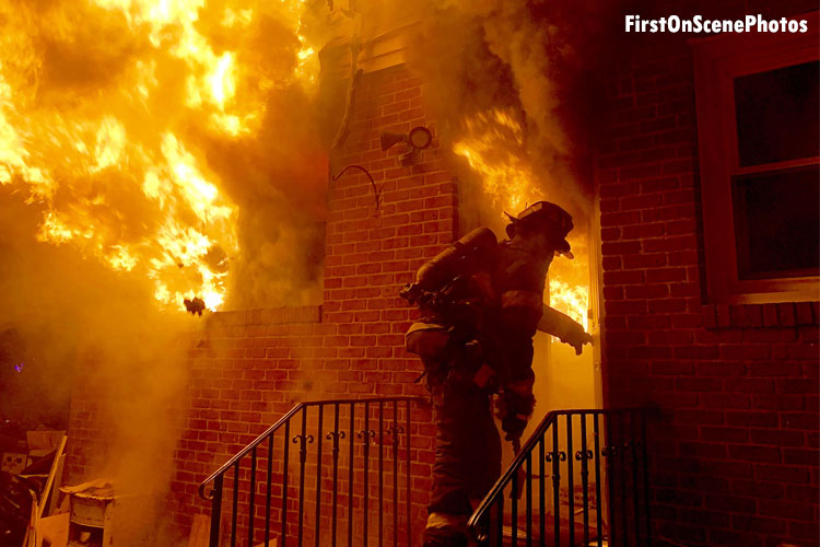 Firefighter making entry to structure as flames shoot from windows