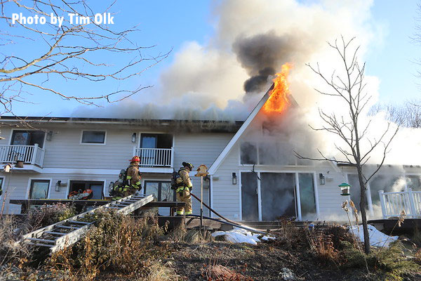 Firefighters pull a line as flames vent from an upper window