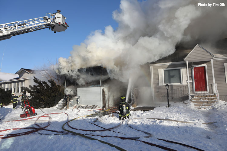 Firefighter with hoseline and firefighter in tower ladder at house fire in snow