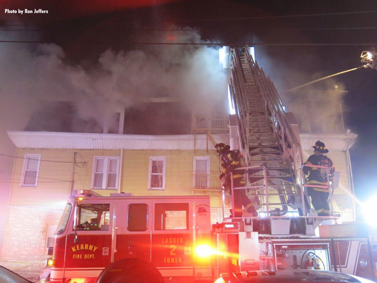 Tower ladder at house fire with firefighters on apparatus