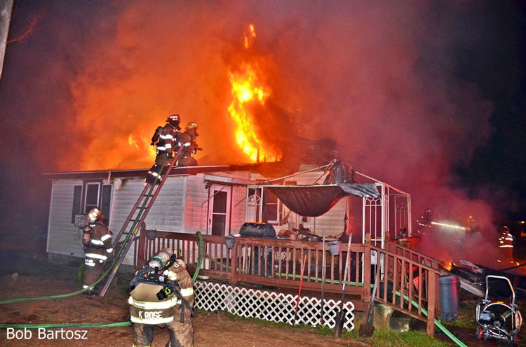 Fire vents through roof of home as firefighters ascend a ladder