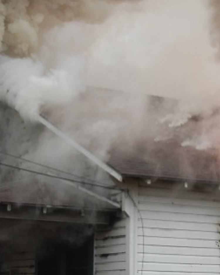 The clean white smoke coming from roofing materials is conductive heating steam, resulting from the fire in the attic space below. (Photo by Dave Dodson.)