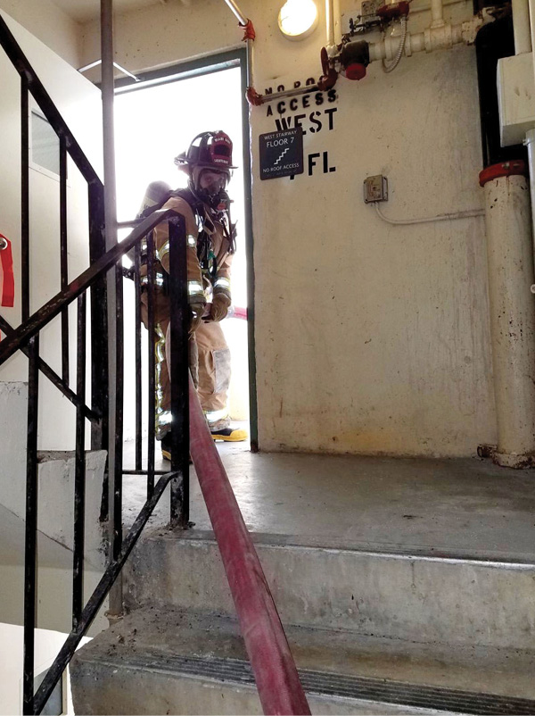 A firefighter positioned at the stairwell’s fire floor landing feeds hose to the firefighters advancing the hoseline down the hallway.