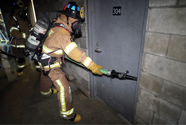 (12) The nozzle team advancing the hoseline first encounters the latch side of the door. The nozzle is jammed against the door frame on the hinged side and 