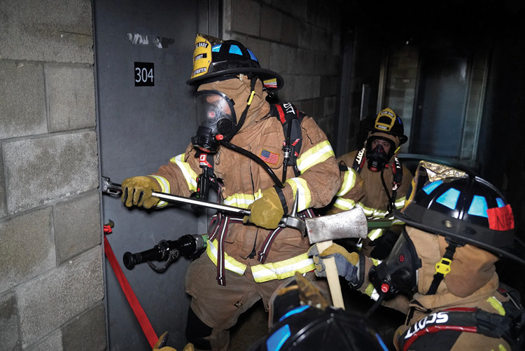 (15) Forcing entry while controlling the door. The nozzle and sufficient hose for its stream to reach any point in the fire compartment are at the ready. 