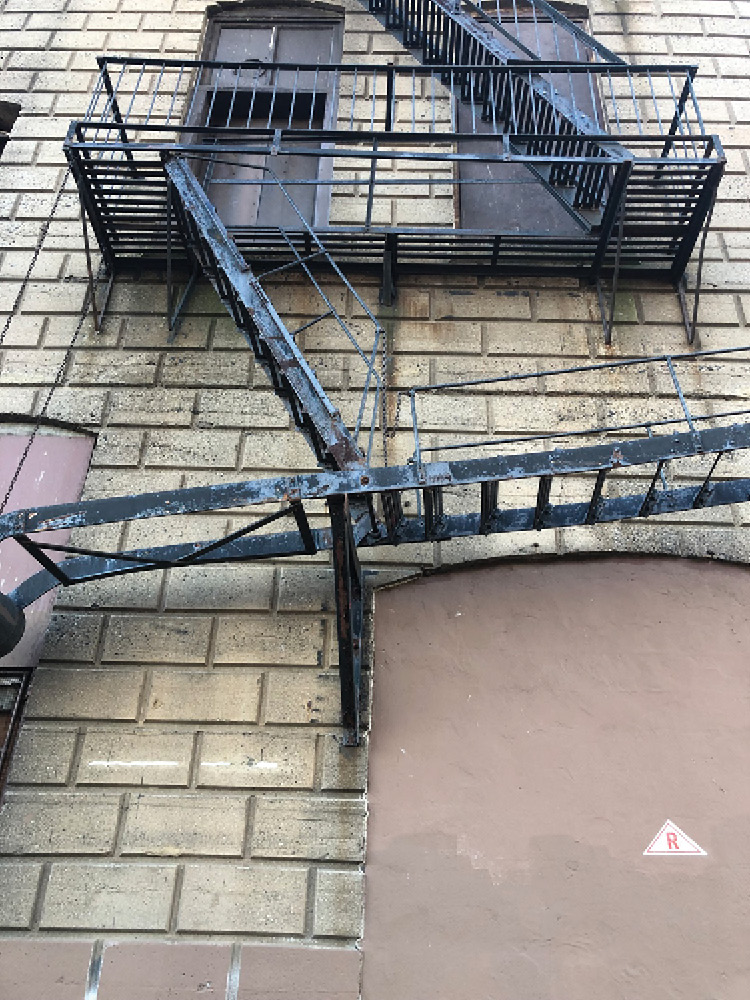 Although not obvious from a distance, the second-floor bracket of this factory fire escape is bent from a (likely) truck impact. A qualified individual must inspect for structural damage of the overall fire escape.