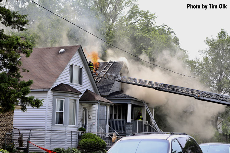 Chicago firefighter on a ladder with fire venting through the roof