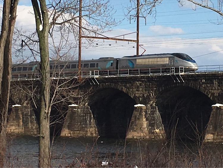 An Amtrak Acela train crossing the Delaware River from Trenton, New Jersey, to Pennsylvania. The size-up for this train should include that it is an “Amtrak high-speed passenger train with an electric locomotive in electrified territory on a bridge over water” followed by the type of emergency (e.g., fire, derailment). This will help determine the type of additional resources needed, the proper command center, and the emergency management contact for removing power and stopping the train.