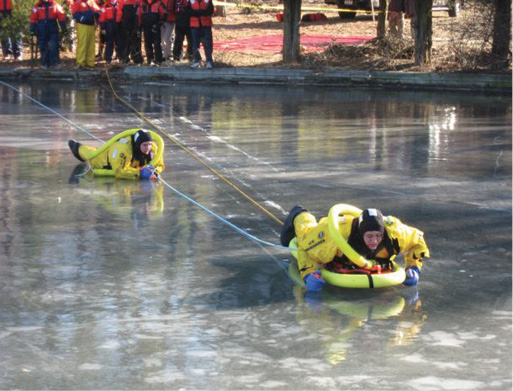 Tech 1 (left) rests on the ice, still connected into the system, while a fresh tech 2 (right) progresses toward the victims. Operations shore personnel control the in and out lines.