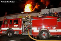 Flames shoot through the roof of the building. An LAFD pumper in the foreground.