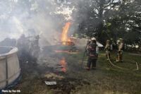 A firefighter applies water to flames burning a vehicle.