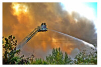 Firefighters in a bucket apply water to the structure fire.