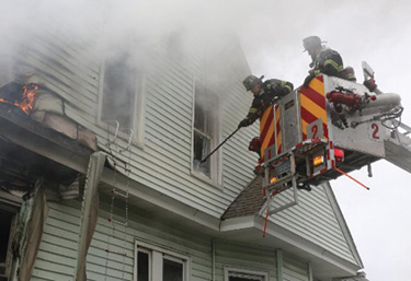 The outside vent firefighter takes an upper-floor window from the bucket of the tower ladder. (Photo by Patrick Dooley.)