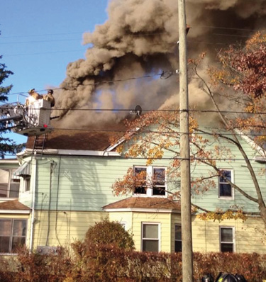 The roof firefighters retreat to the bucket after cutting a vent hole in the roof over a well-involved attic fire. (Photo by Kevin Klett.)