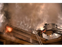 Firefighters make the roof as fire vents from the home.