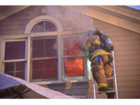 Fire rages inside the home as a firefighter operates on a ladder.